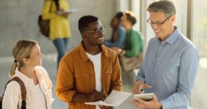 Avaliação dos docentes de Programas de Pós-graduação - Estudantes felizes e seu professor usando o touchpad no corredor da universidade